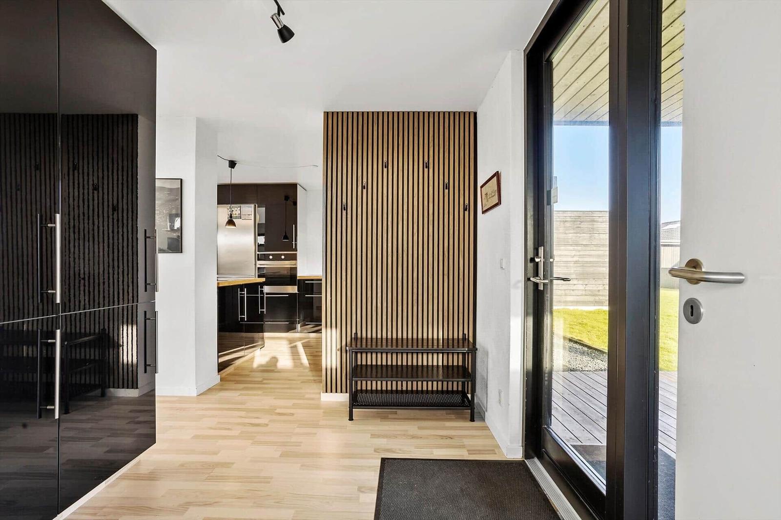 Entryway with wooden floor, wood panel wall, and view into the kitchen.