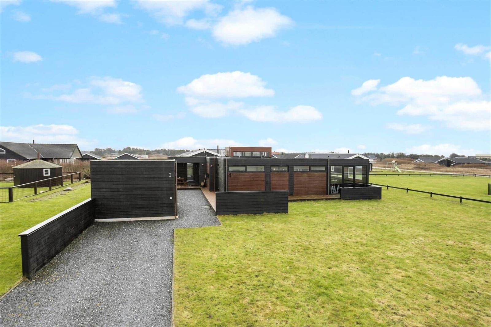 Modern villa with wooden facade and large garden under blue sky.