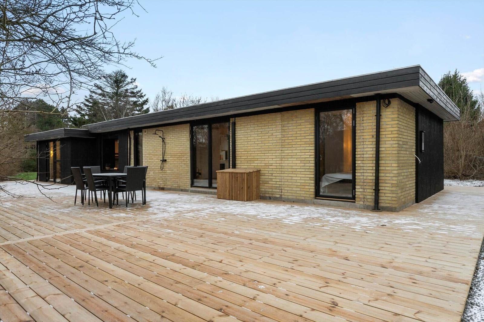 Modern holiday home with terrace, table, chairs, and wooden sauna.