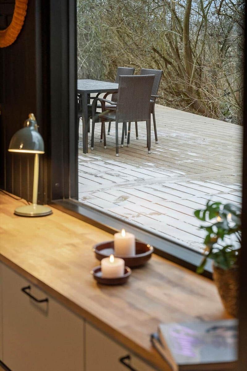Through the window, a terrace with a table and chairs is visible. In the foreground, candles burn on a worktop.