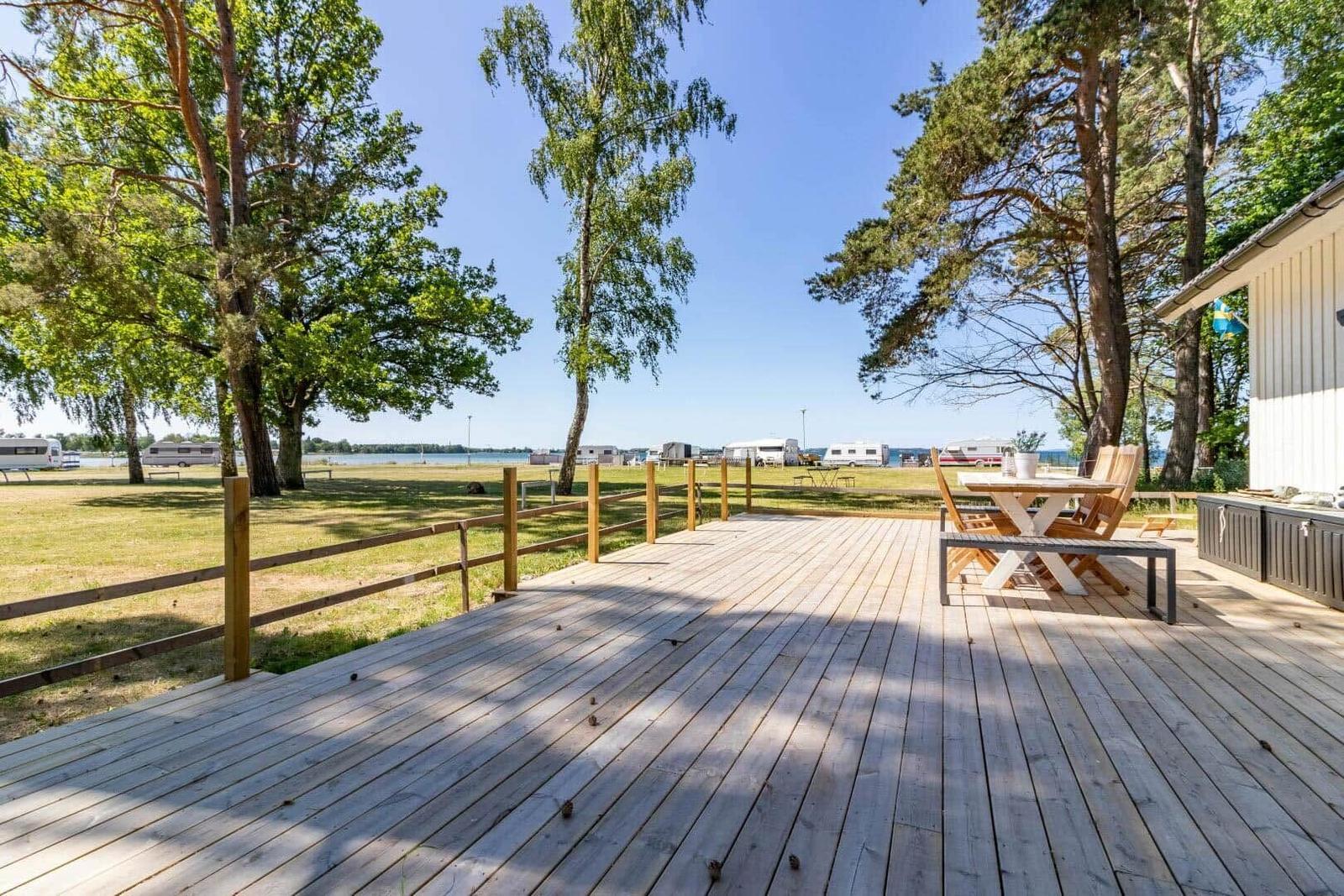 Holzterrasse mit Tisch und Stühlen, Blick auf Grünfläche und See.
