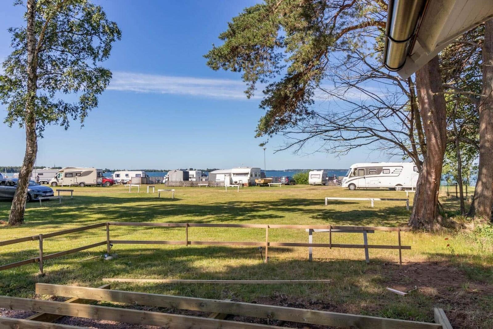 Grüner Campingplatz mit Wohnmobilen am Wasser unter Bäumen.