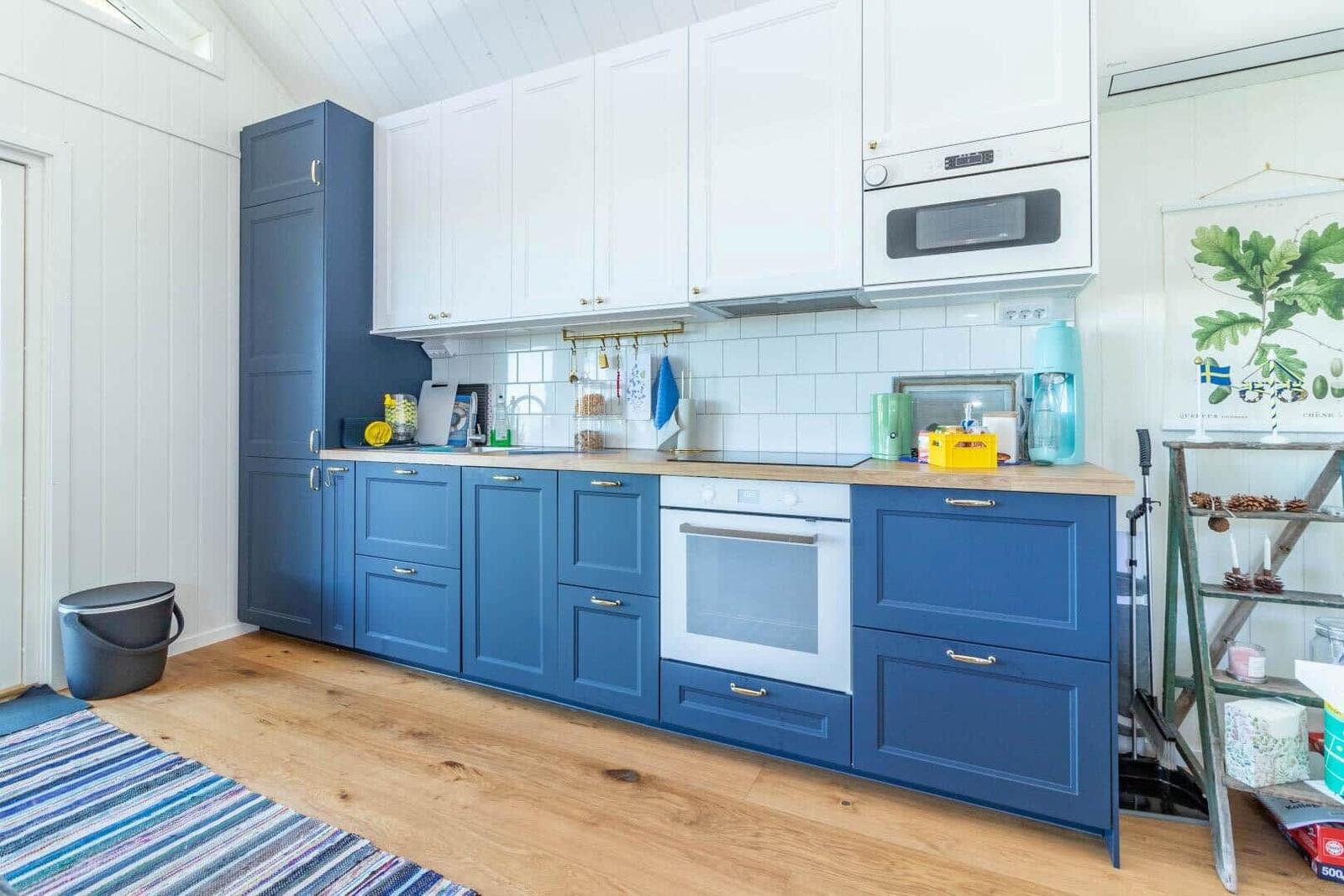 Küche mit blauen und weißen Schränken, Holzboden und weißer Fliesenwand.