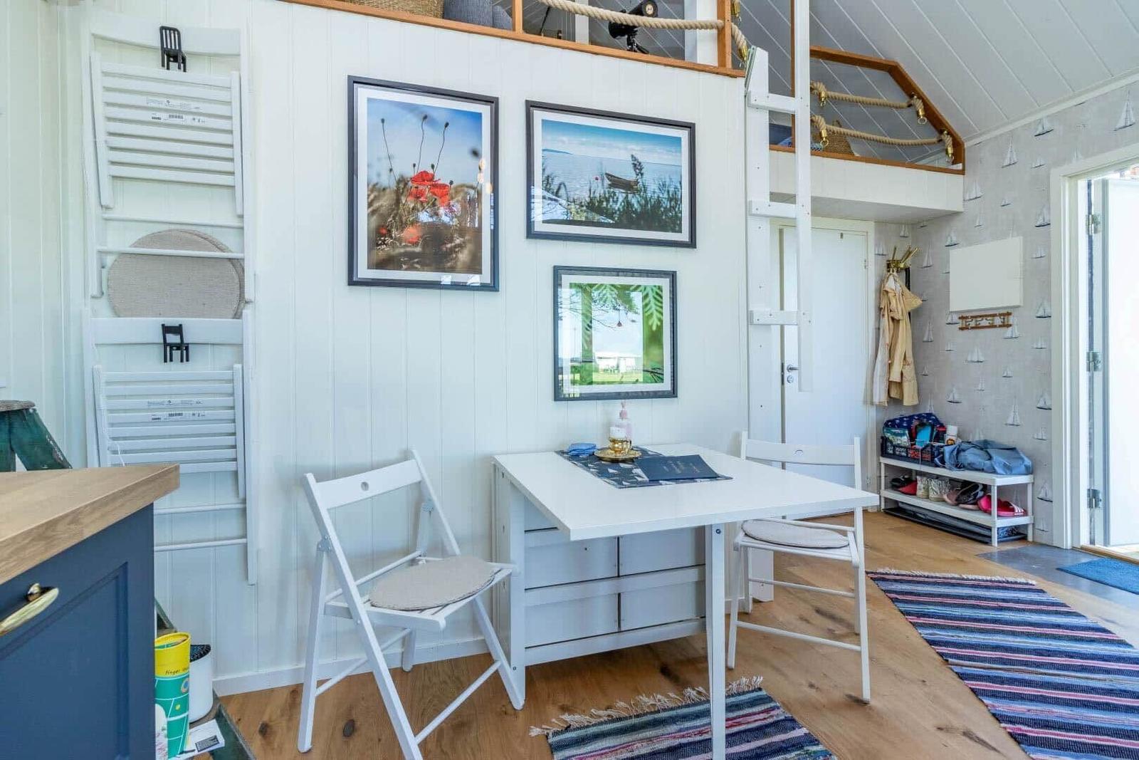 Wohnraum mit Tisch, Stühlen und Wandbildern. Oben befindet sich eine Galerie mit Leiter.