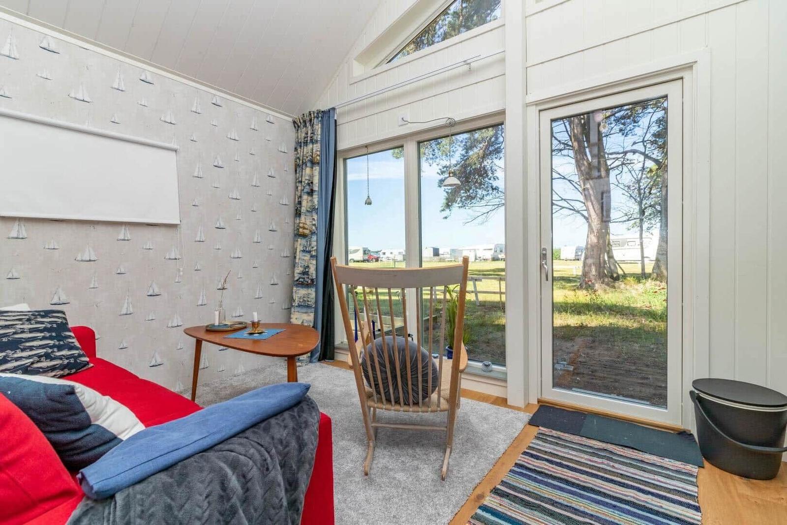Ein Raum mit rotem Sofa, Holzstuhl und großem Fenster zur Außenterrasse.