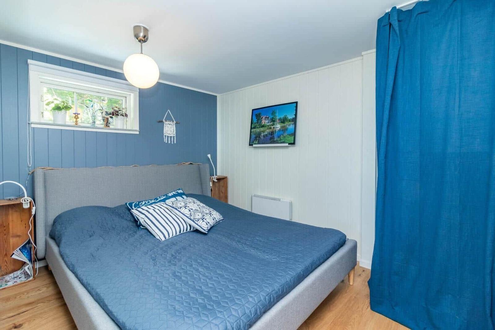 Schlafzimmer mit blauer Wand, Bett und TV. Holzfußboden und blaue Vorhänge.