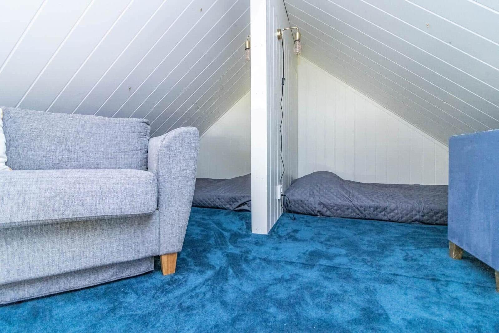 Zimmer mit grauem Sofa, blauem Teppich und Bett unter Dachschrägen.