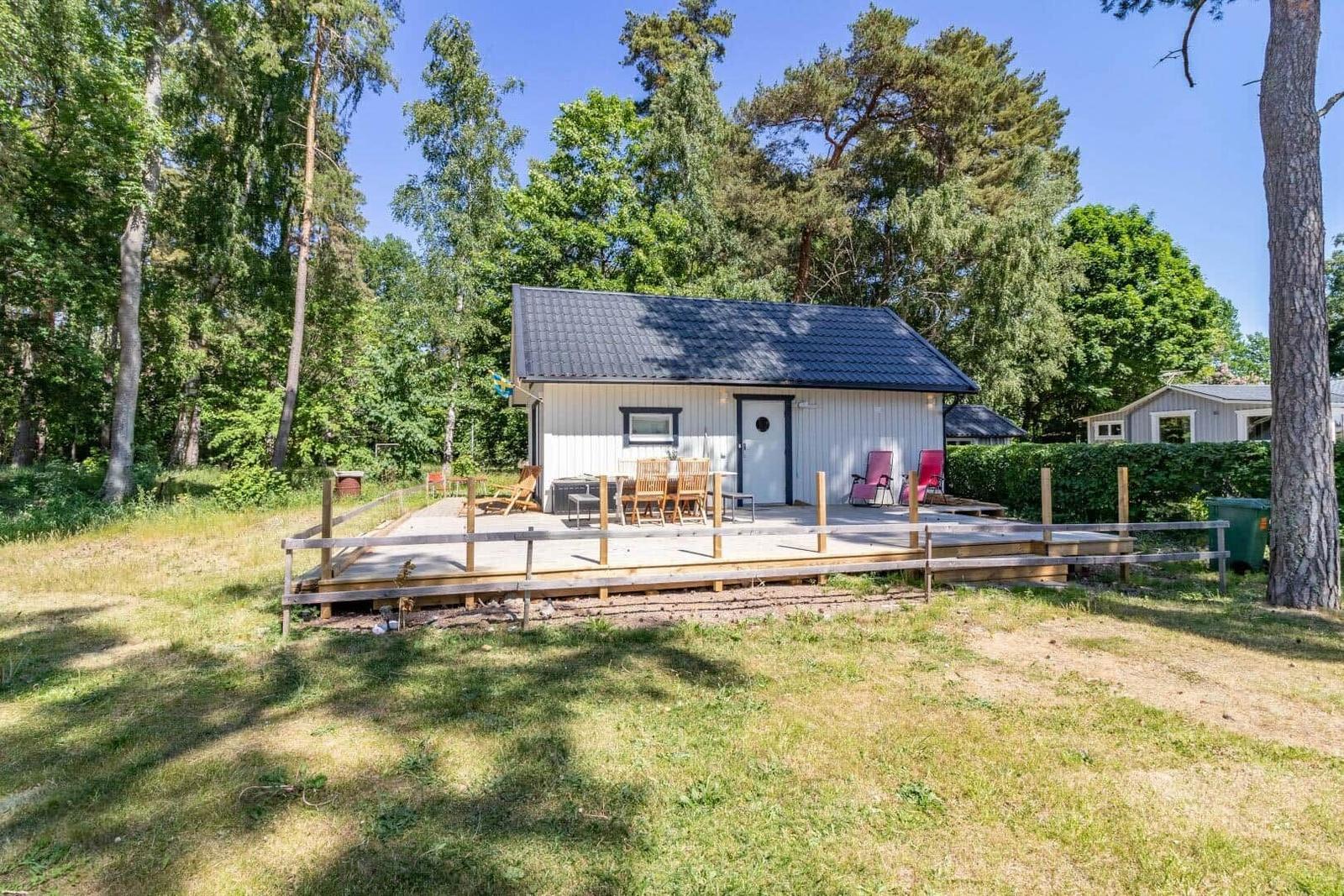 Ein kleines Haus mit Terrasse, Garten und Bäumen im Hintergrund.