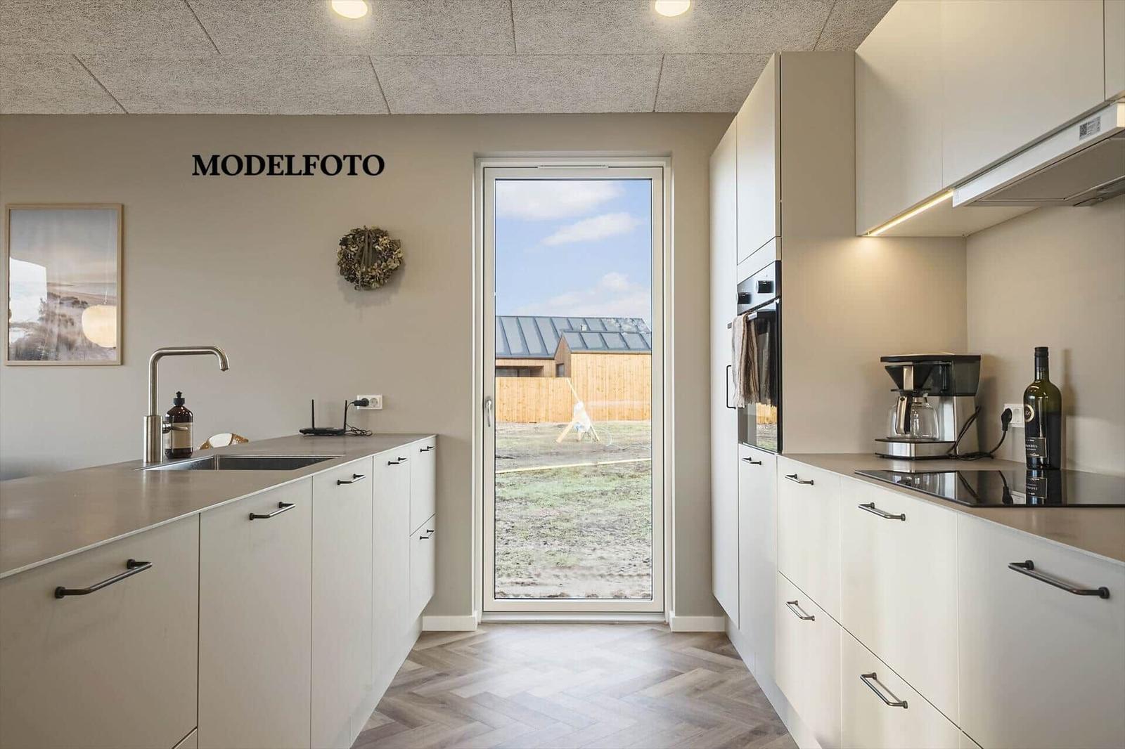 Moderne Küche mit Blick auf den Garten. Weiße Schränke, Edelstahlspüle und Kaffeemaschine.