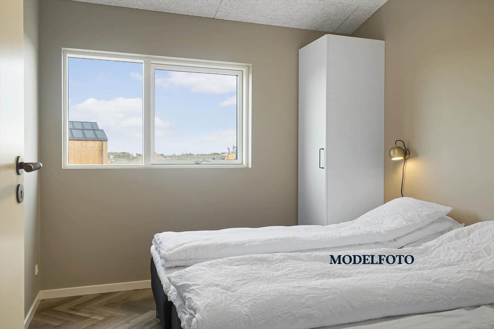 Schlafzimmer mit weißem Bett, Kleiderschrank und Fenster mit Blick.