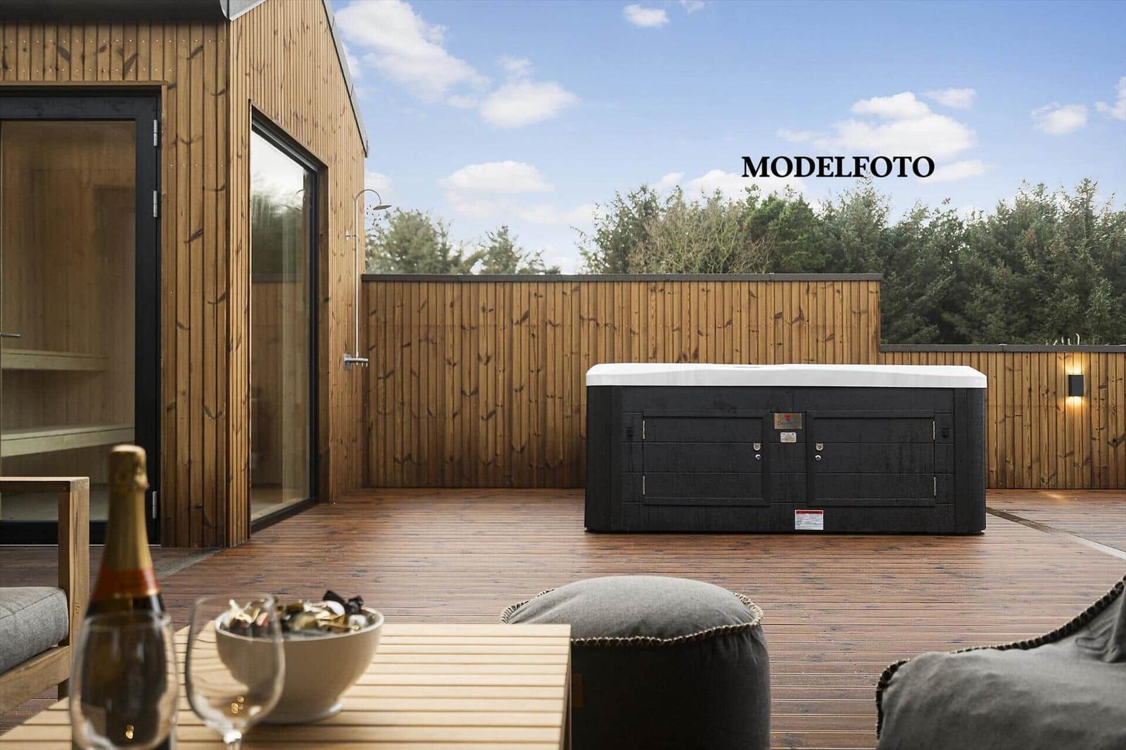Terrasse mit Whirlpool, Sitzgelegenheiten und Sauna. Holzgeländer und Himmel mit Wolken.