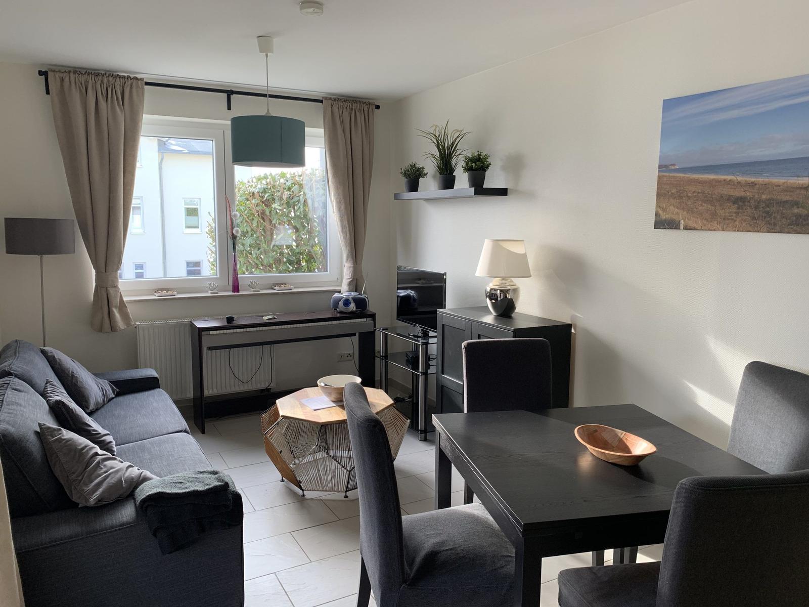 Wohnzimmer mit Sofa, Esstisch und Fenster. Wandbild zeigt Strand.