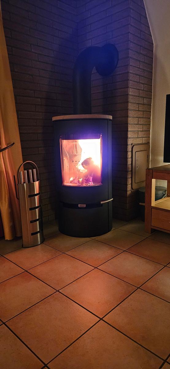 Holzofen mit brennendem Feuer in Ecke mit Ziegelwand und Fliesenboden.