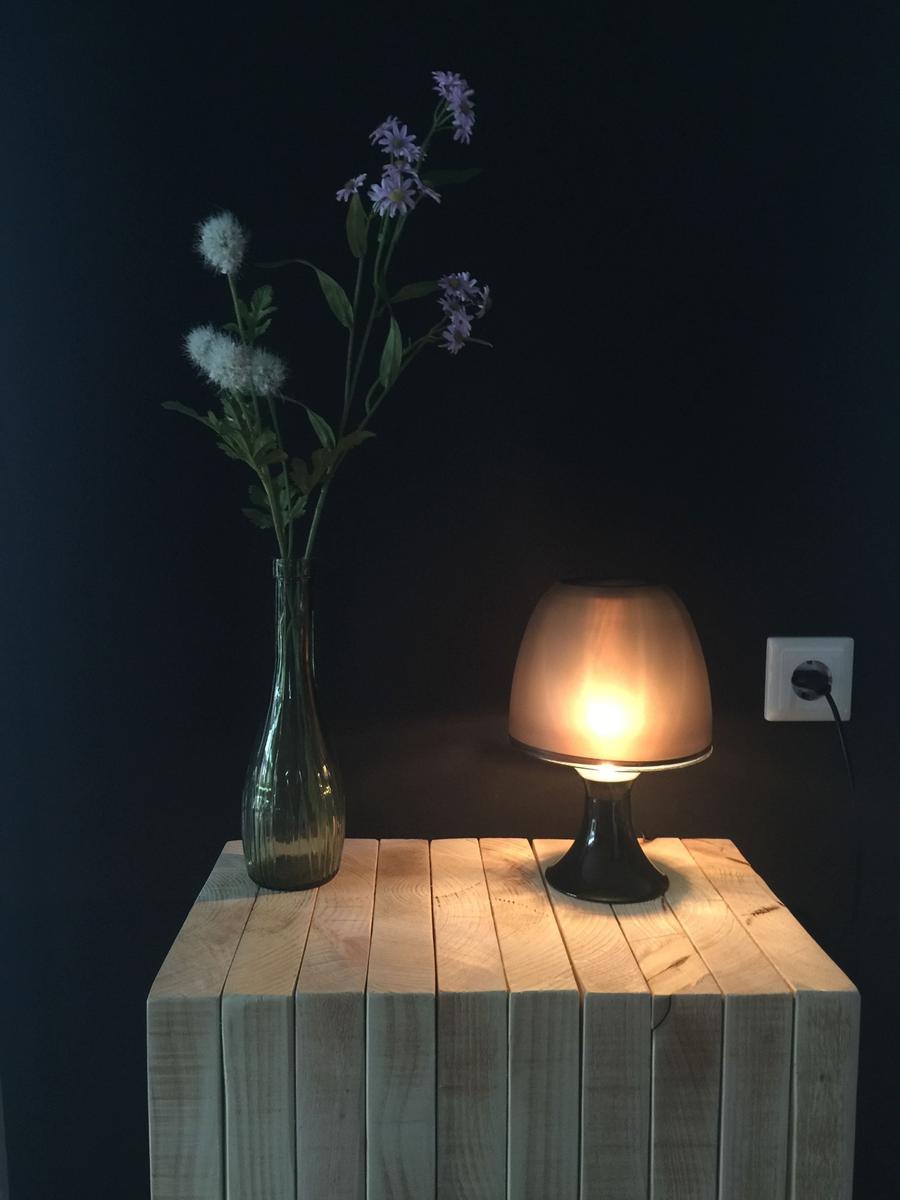 Auf einem Holztisch steht eine Lampe und ein Glasvasen mit Blumen.