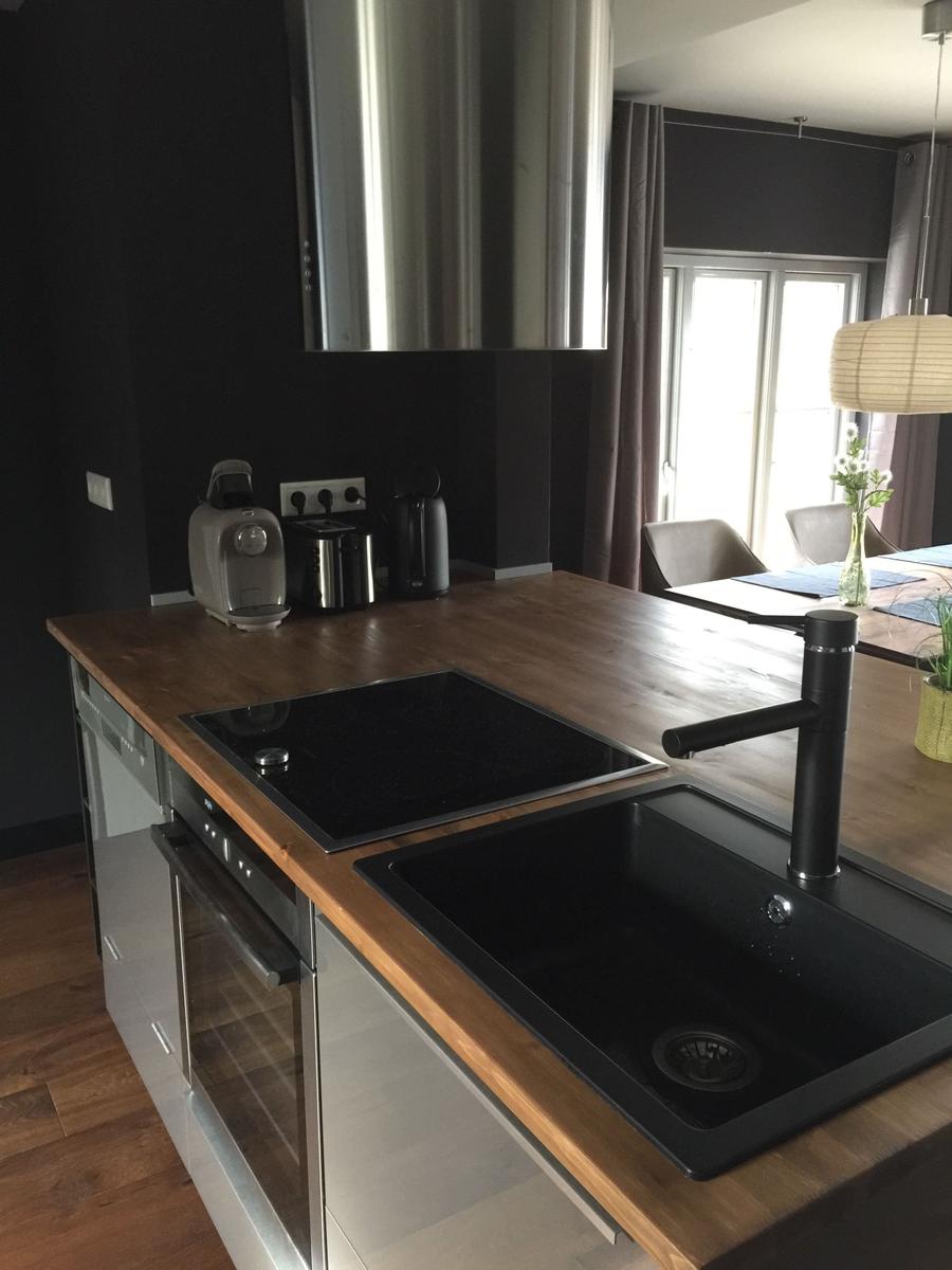 Küche mit Holzplatte, Kochfeld und Spüle. Hintergrund zeigt Essbereich.