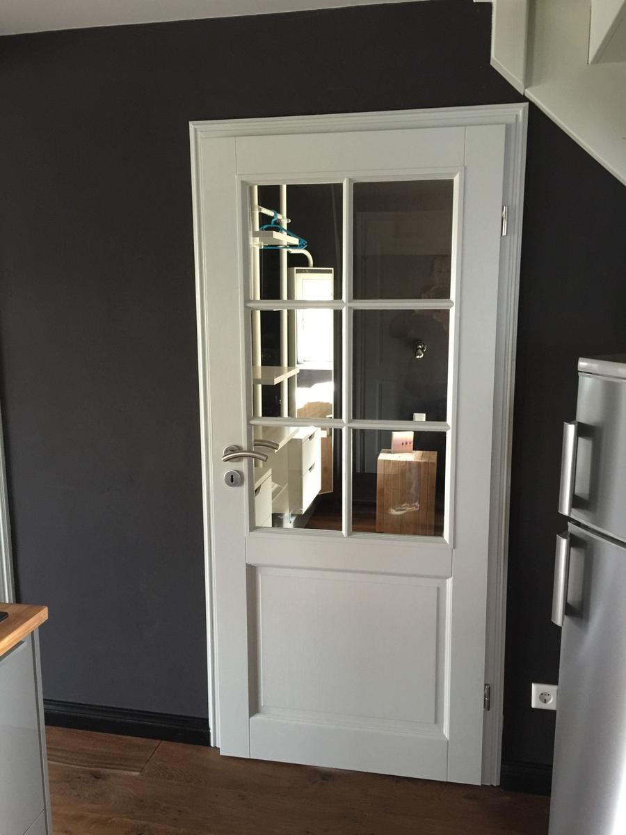 Weiße Tür mit Glasfenstern führt in einen Raum mit Kleiderschrank und Holzbox.