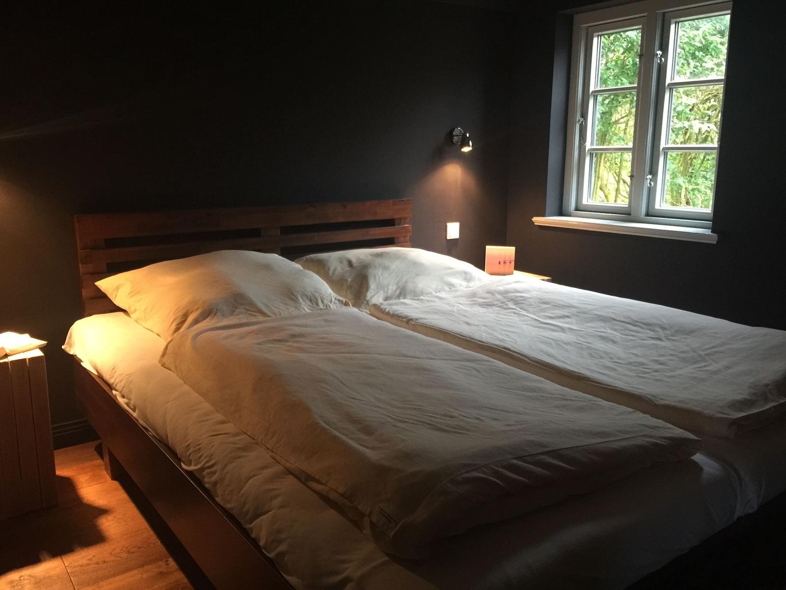 Schlafzimmer mit Doppelbett, Holzrahmen und Fenster mit Blick auf Bäume.