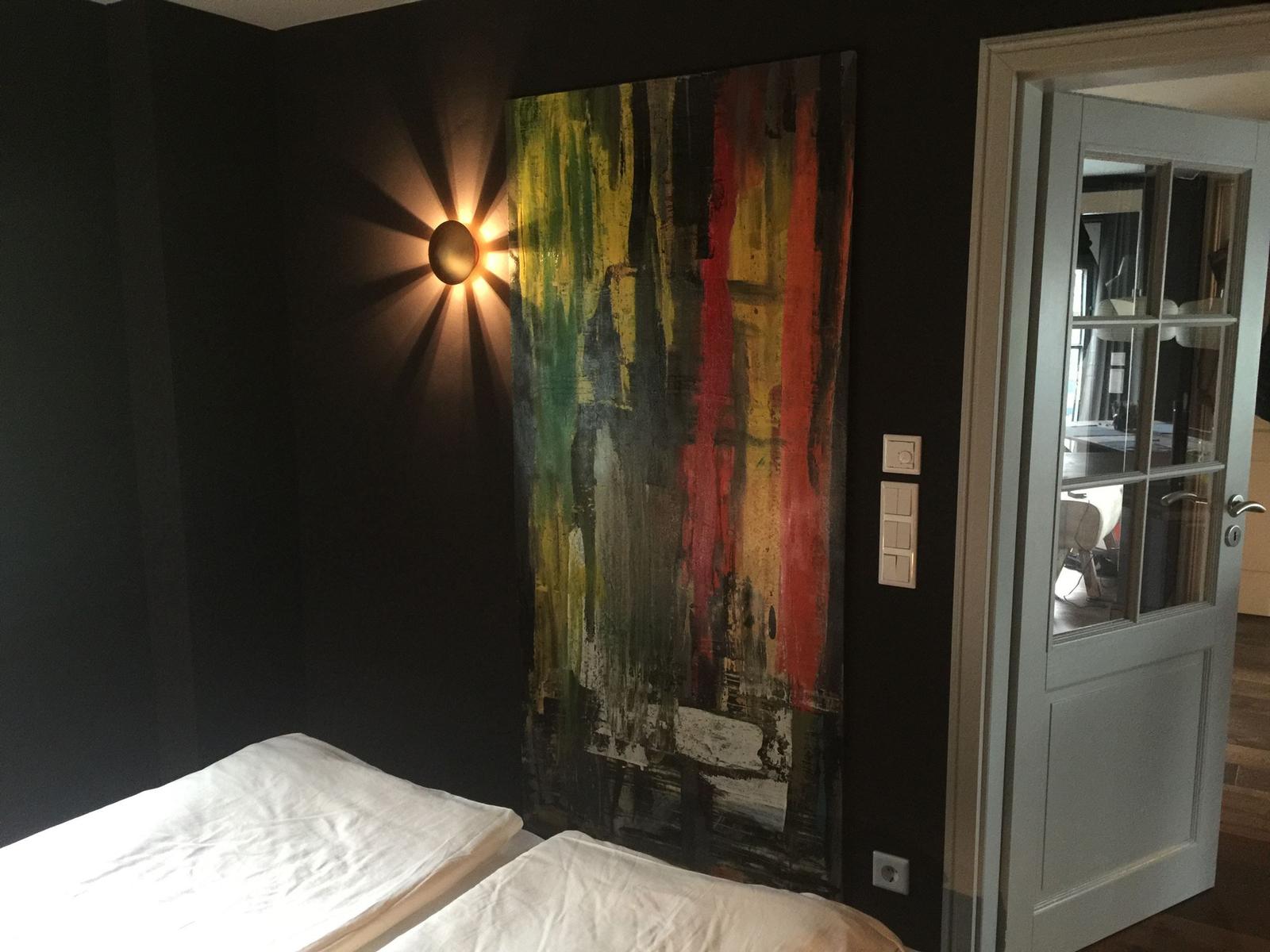 Schlafzimmer mit Bett, Wandbild und Nachttischlampe. Tür führt in angrenzenden Raum.