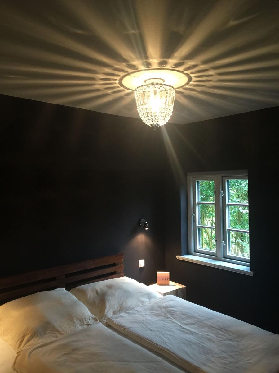 Schlafzimmer mit Bett, Fenster und Kristalldeckenleuchte.