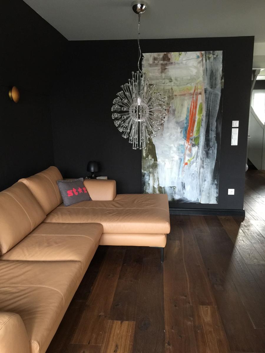 Ein Wohnzimmer mit braunem Sofa, dunkler Wand und Glasleuchte.