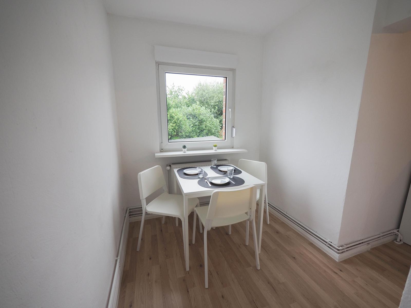 Essbereich mit weißem Tisch und Stühlen, Fenster mit Blick auf Grün.