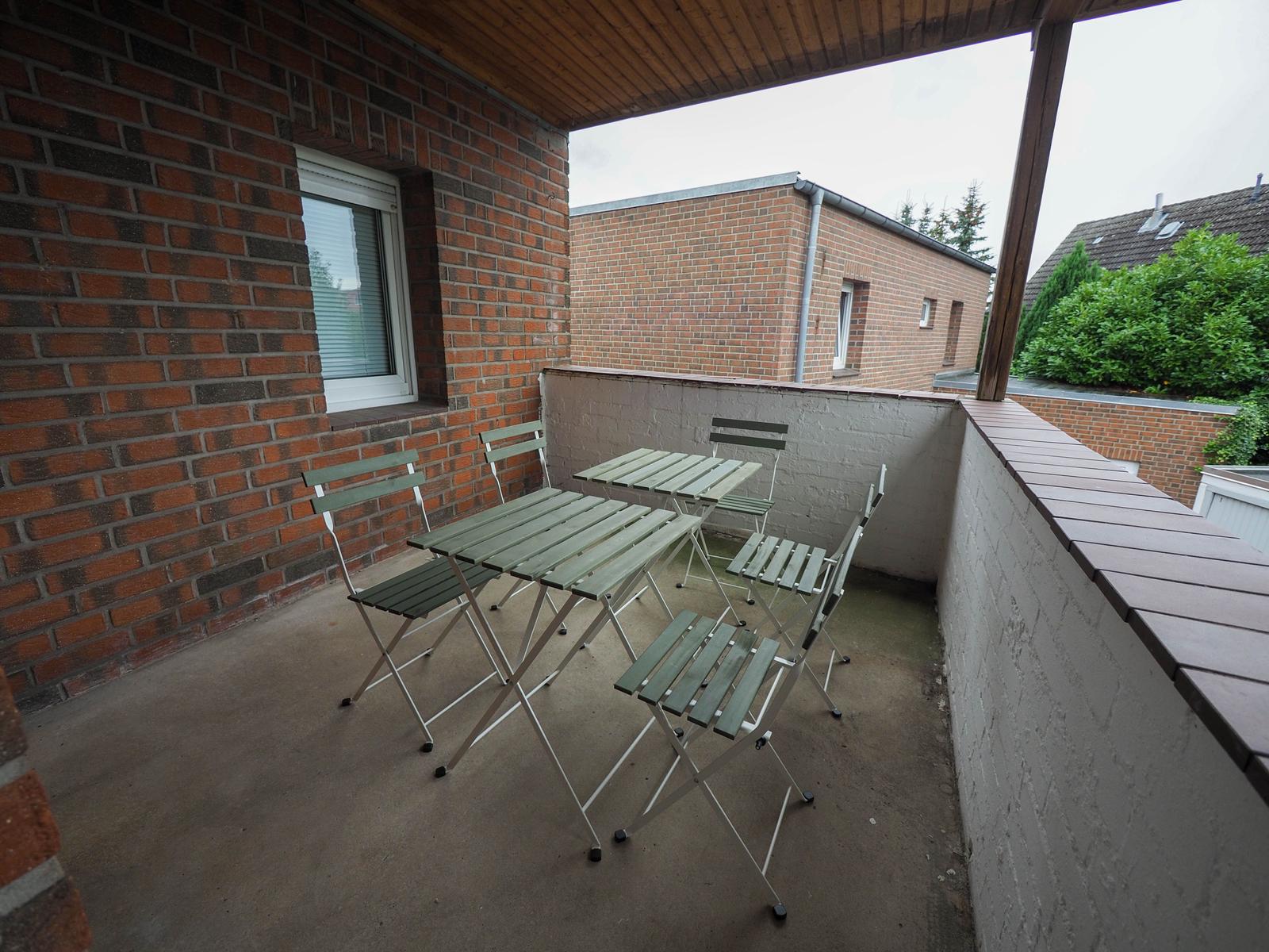 Terrasse mit Tisch und Stühlen, Blick auf Nachbarhäuser und Grünflächen.