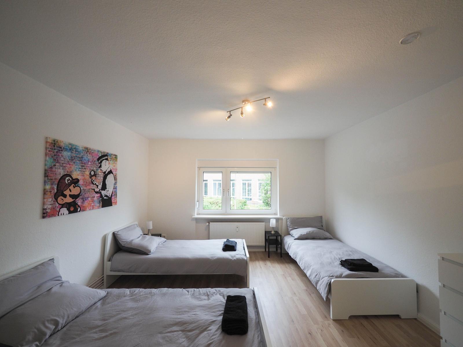 Zimmer mit drei Betten, Fenster und Wandbild.