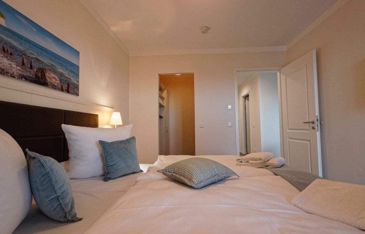 Schlafzimmer mit Bett, Kissen und Wandbild. Tür führt in angrenzenden Raum.