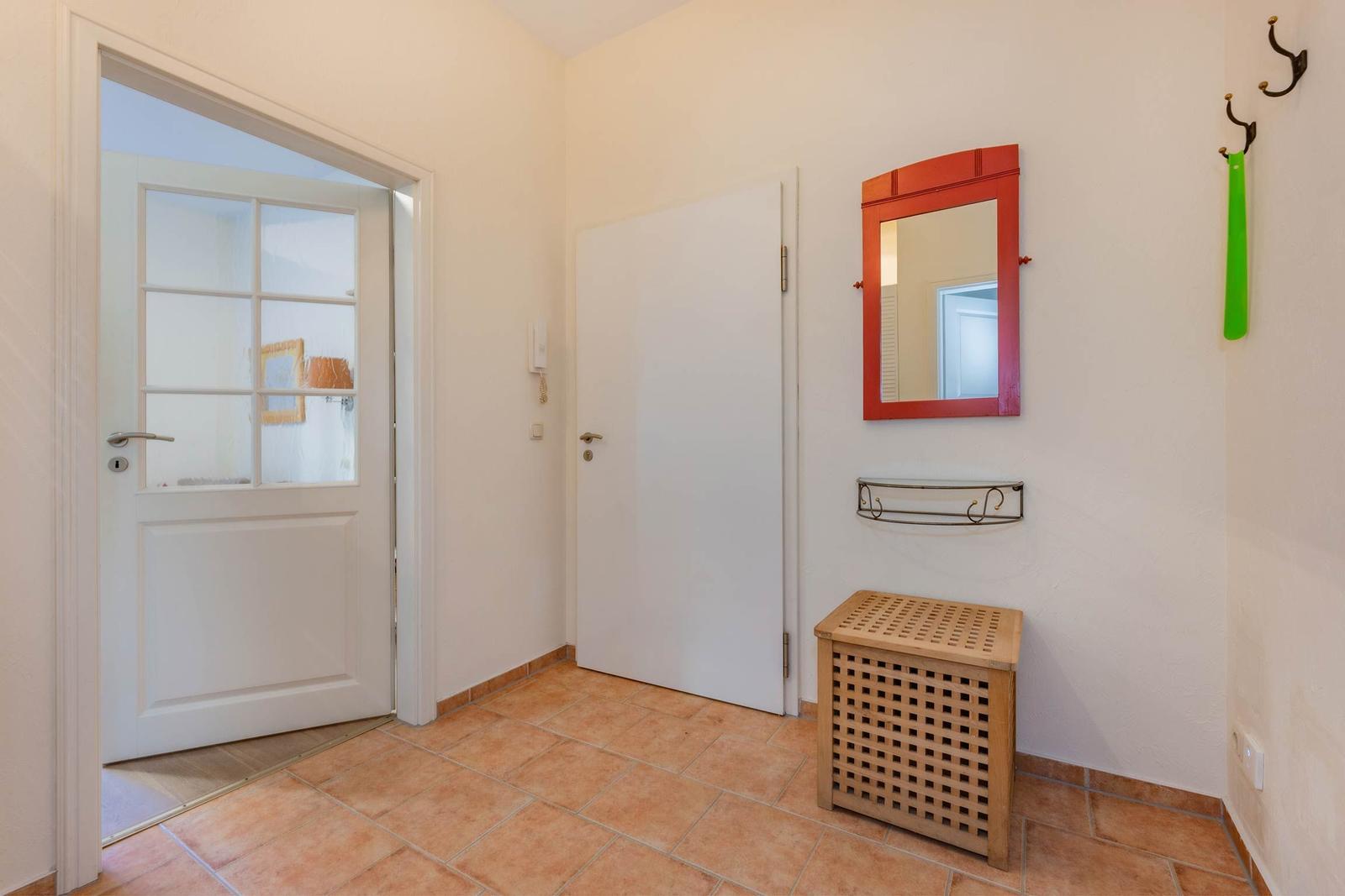 Eingangsbereich mit Holzbank, Spiegel und Haken an der Wand.