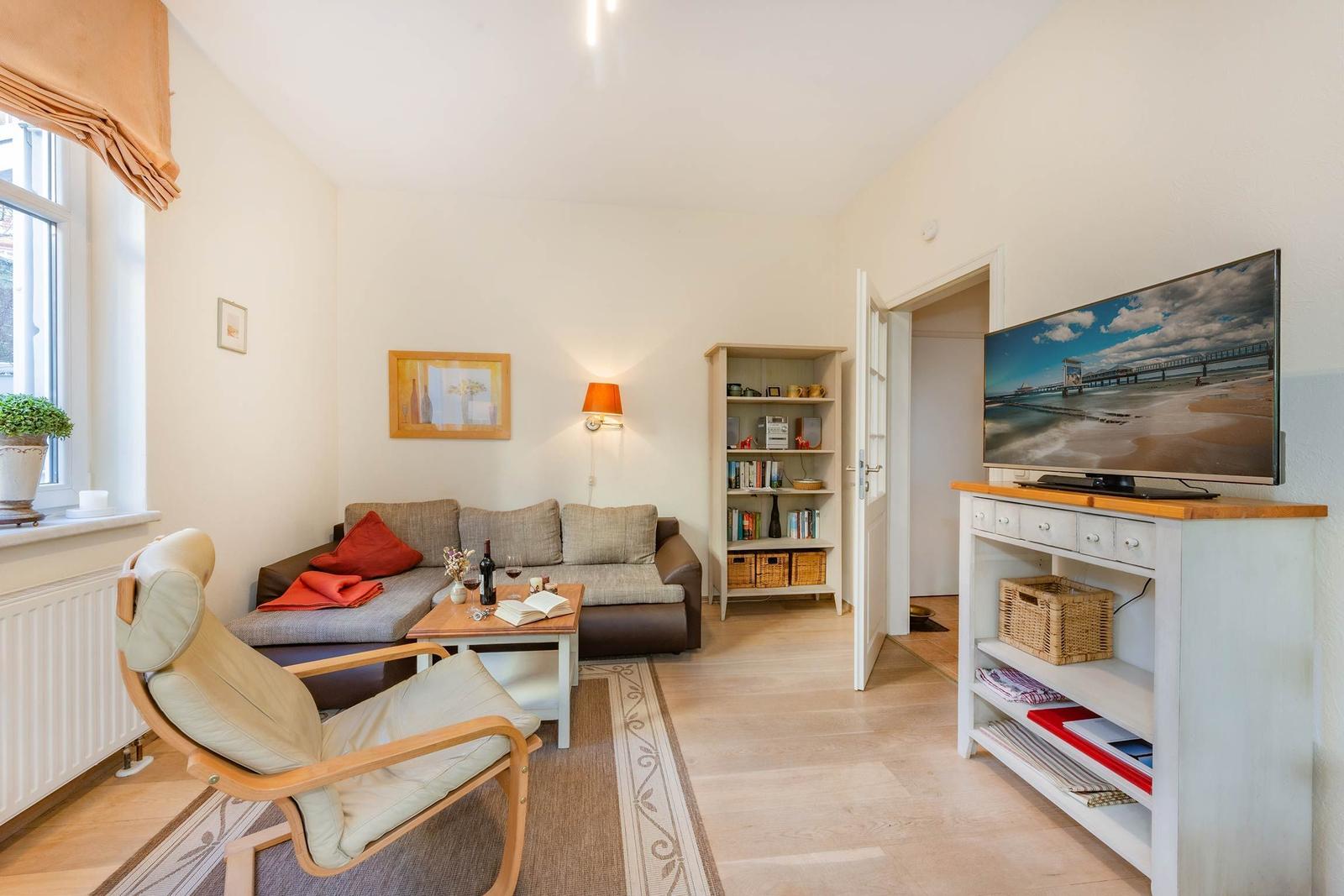 Wohnzimmer mit Sofa, Sessel, Fernseher und Bücherregal.