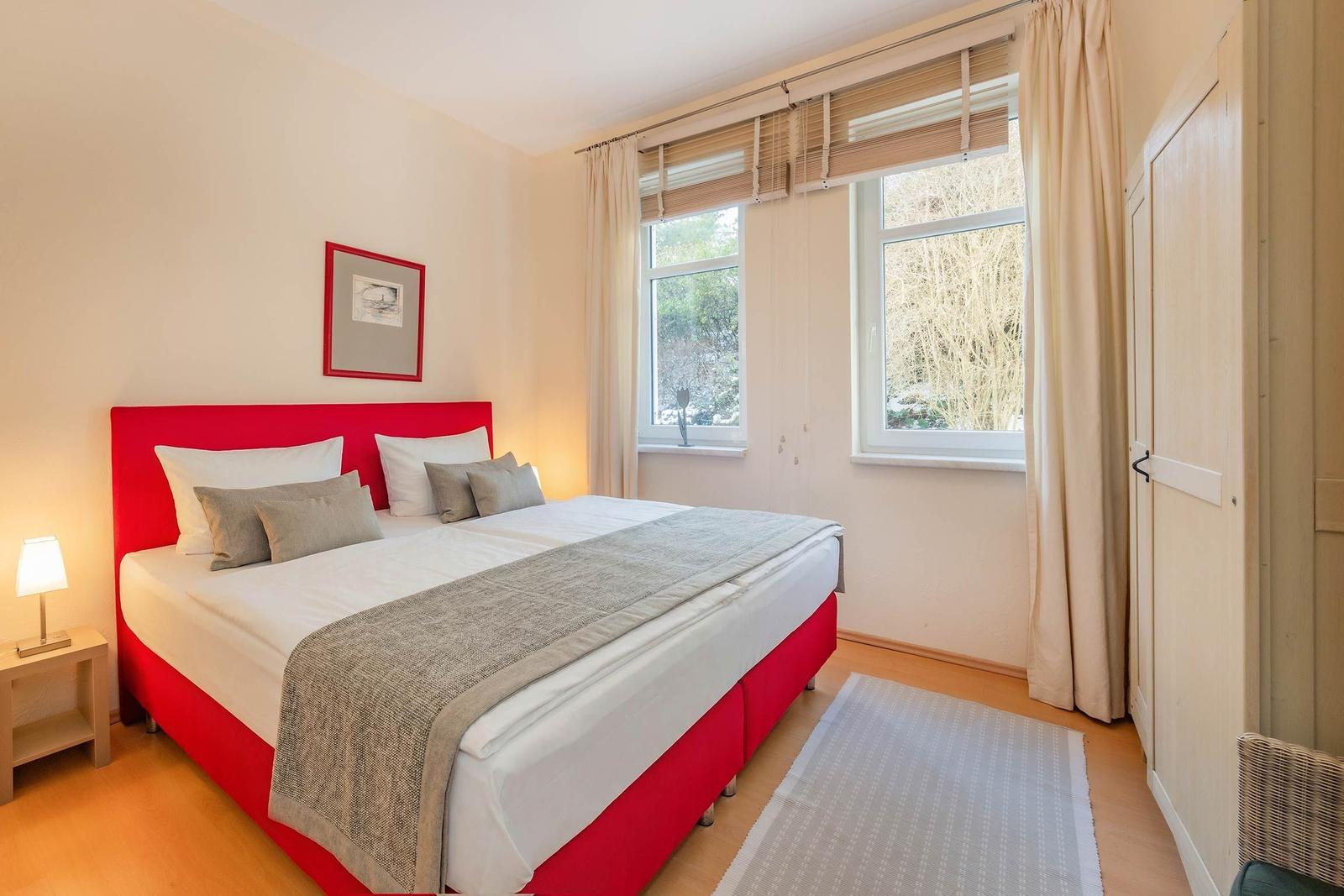 Schlafzimmer mit rotem Bett, Fenster und Kleiderschrank.