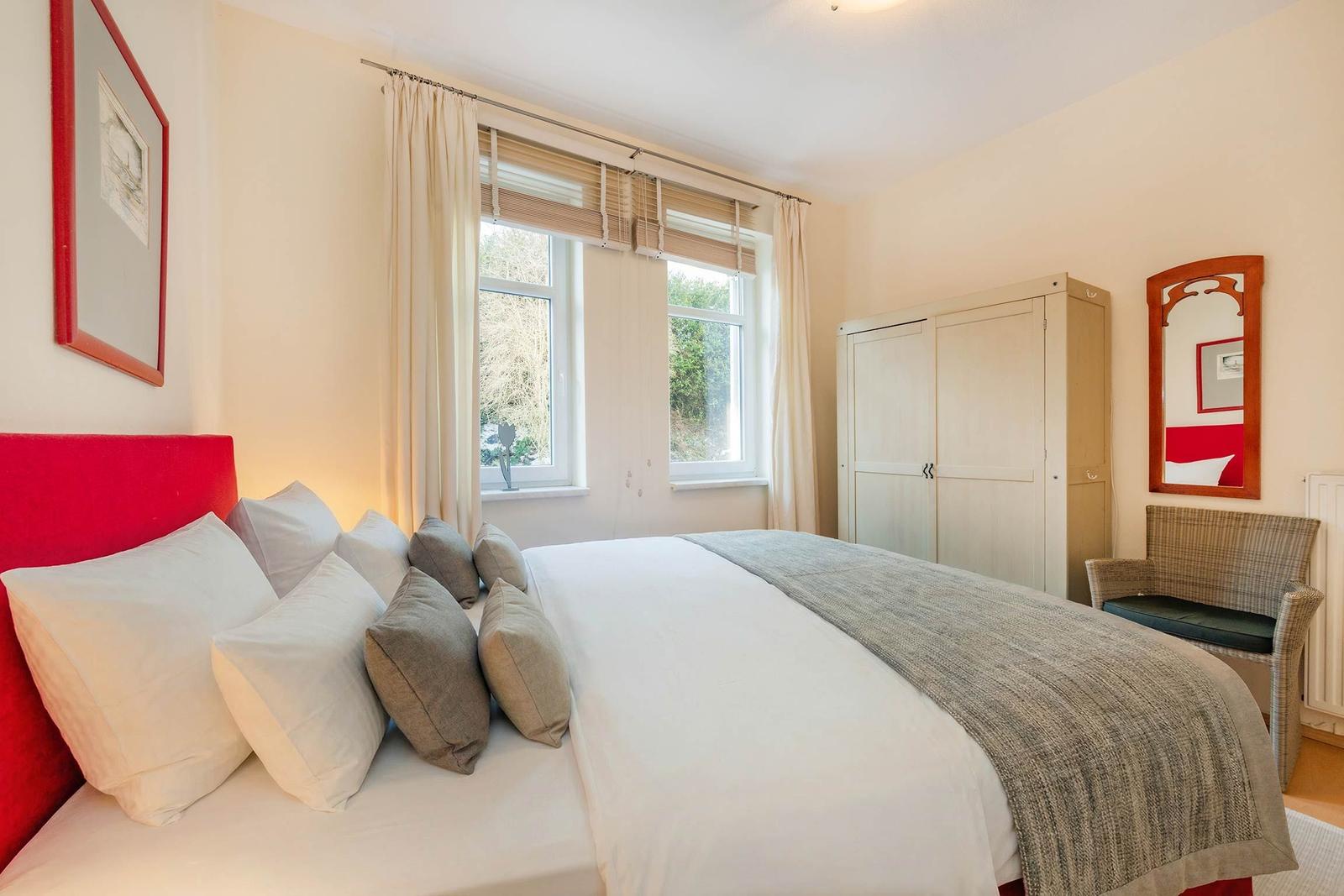 Schlafzimmer mit Bett, Kleiderschrank und Fenster mit Blick auf Grün.