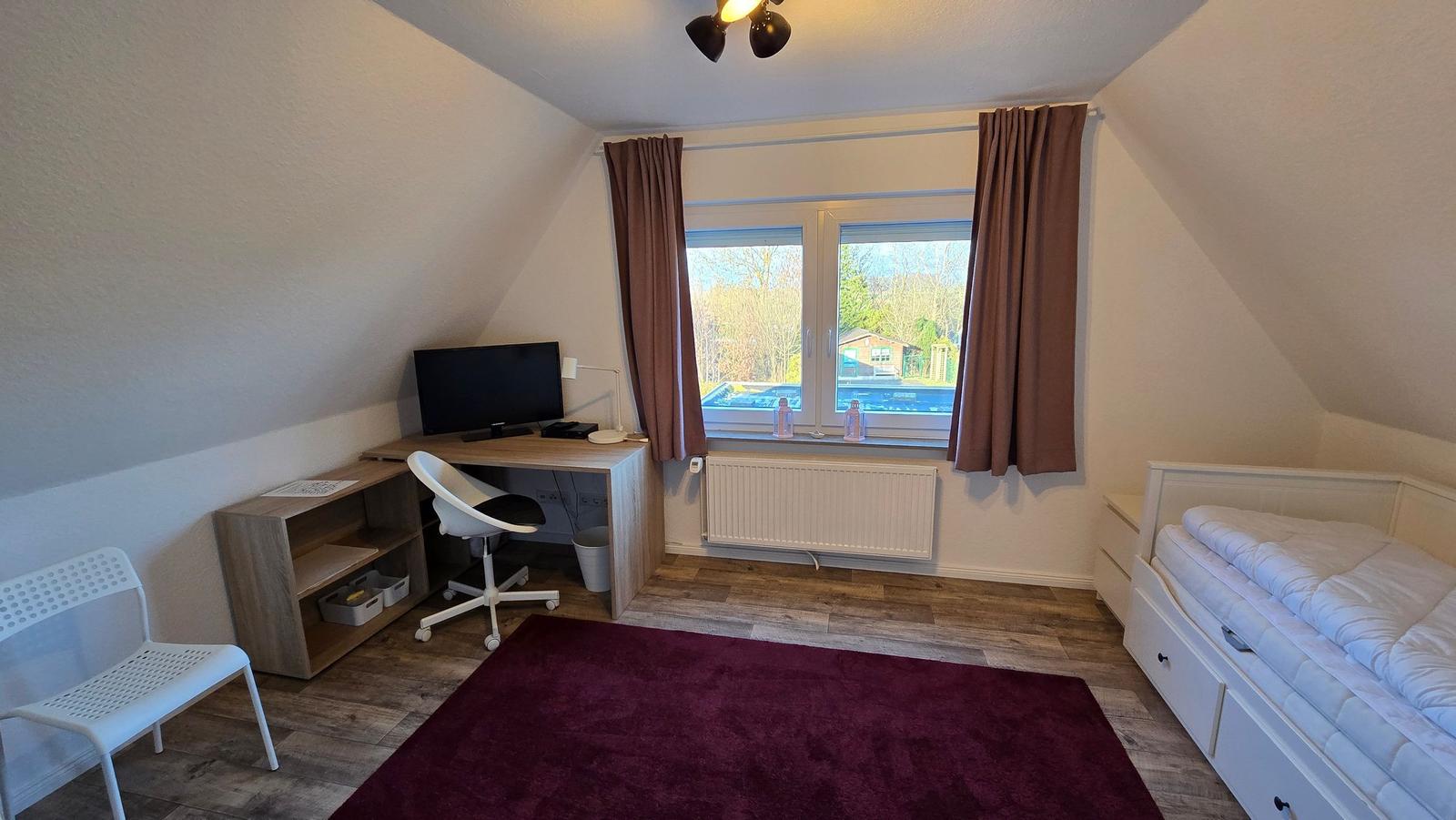 Schlafzimmer mit Bett, Schreibtisch, Fenster und Teppich.