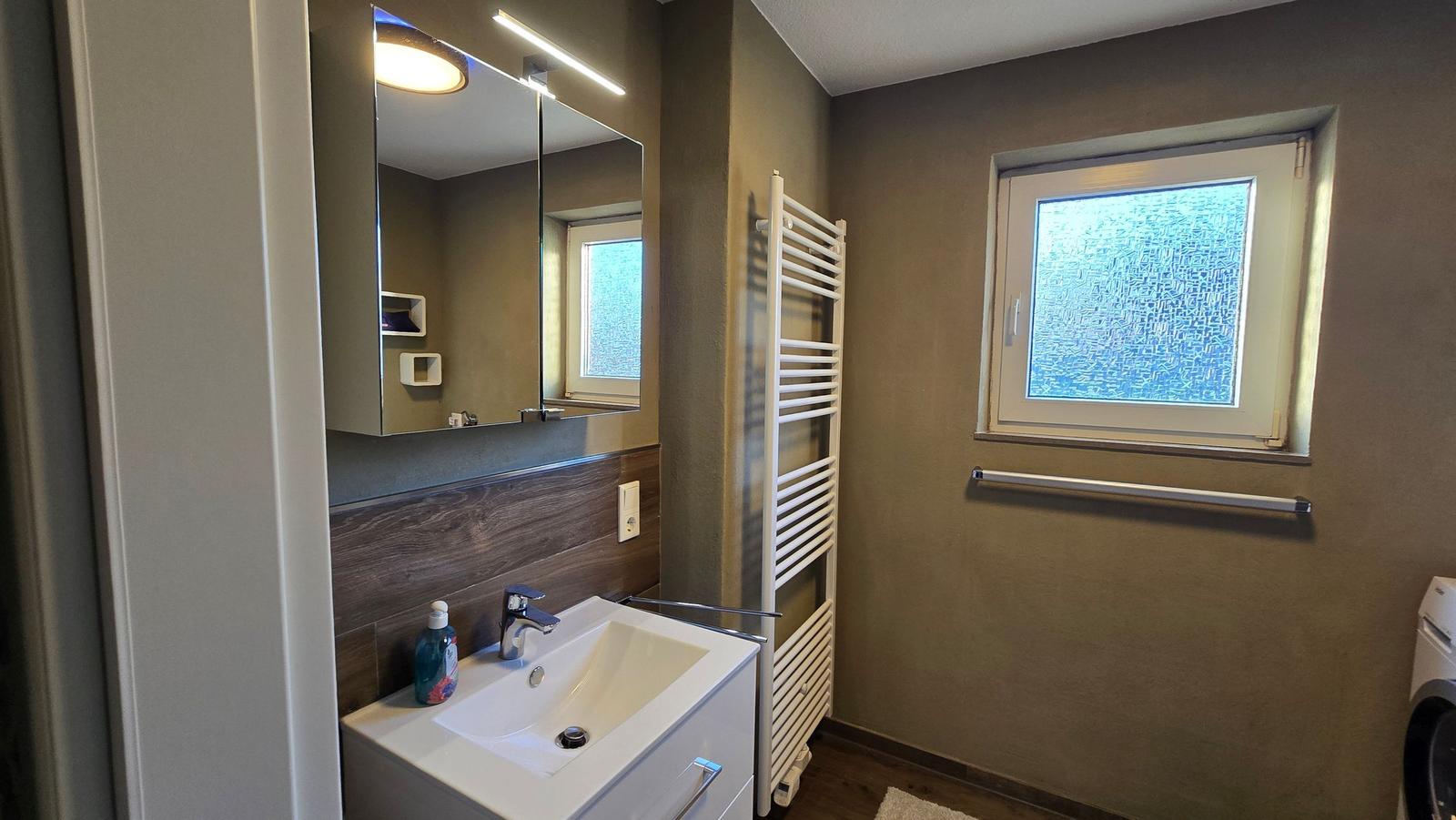 Badezimmer mit Waschbecken, Spiegel und Fenster.