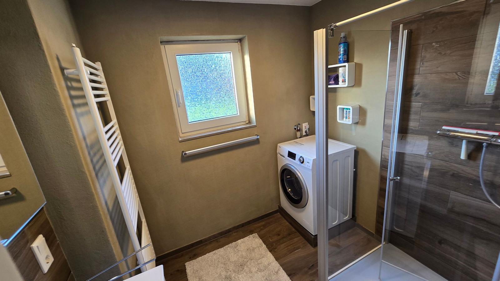 Badezimmer mit Dusche, Waschmaschine und Heizkörper.