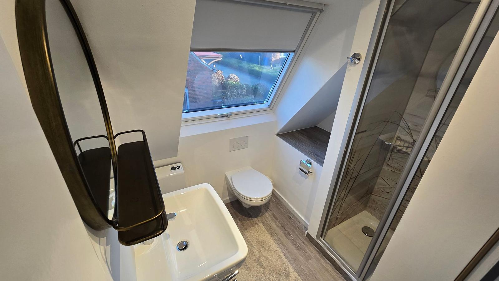 Badezimmer mit Dusche, WC und Waschbecken unter Dachfenster.