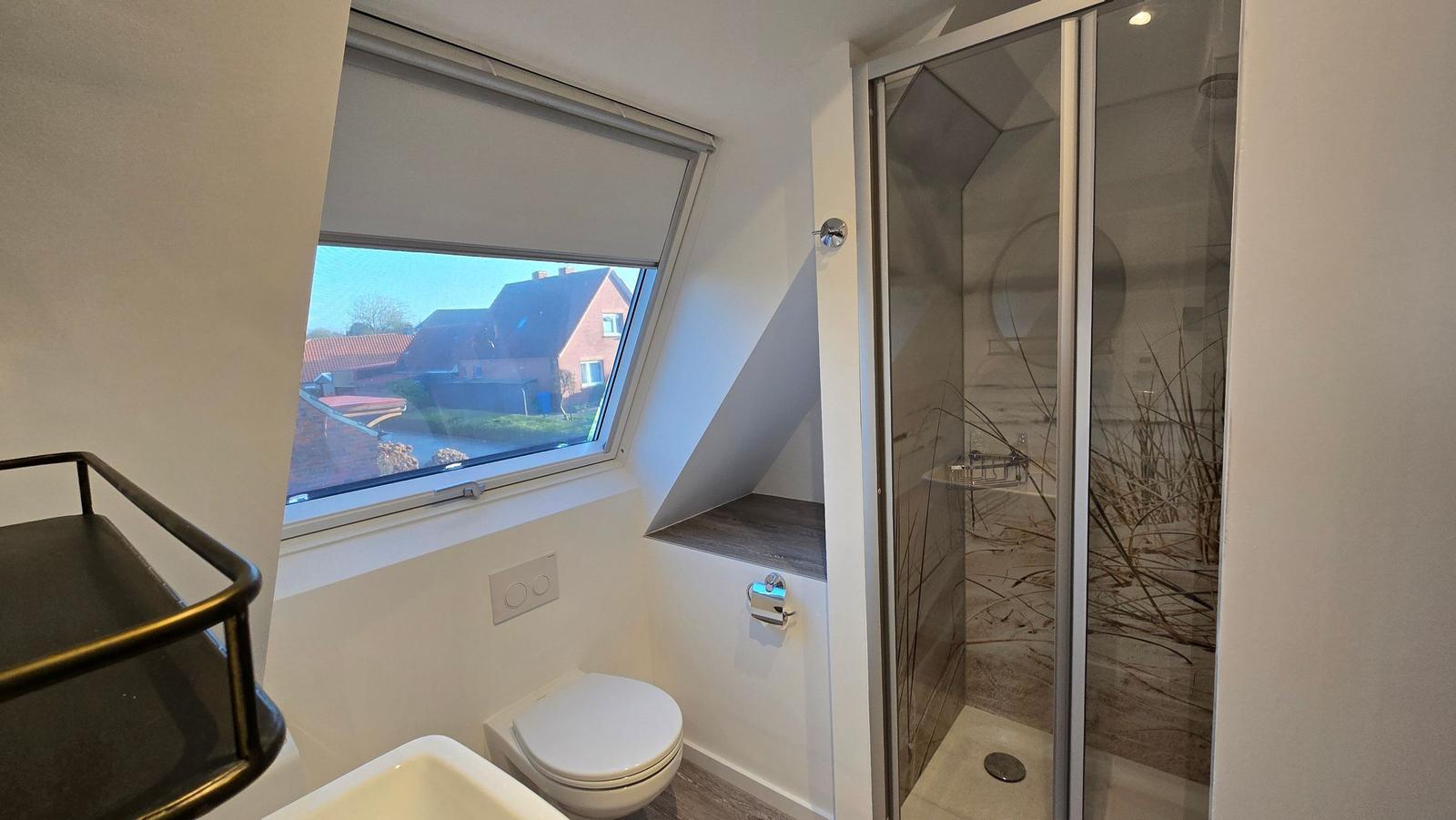 Badezimmer mit Dusche, Toilette und Dachfenster mit Blick auf die Umgebung.