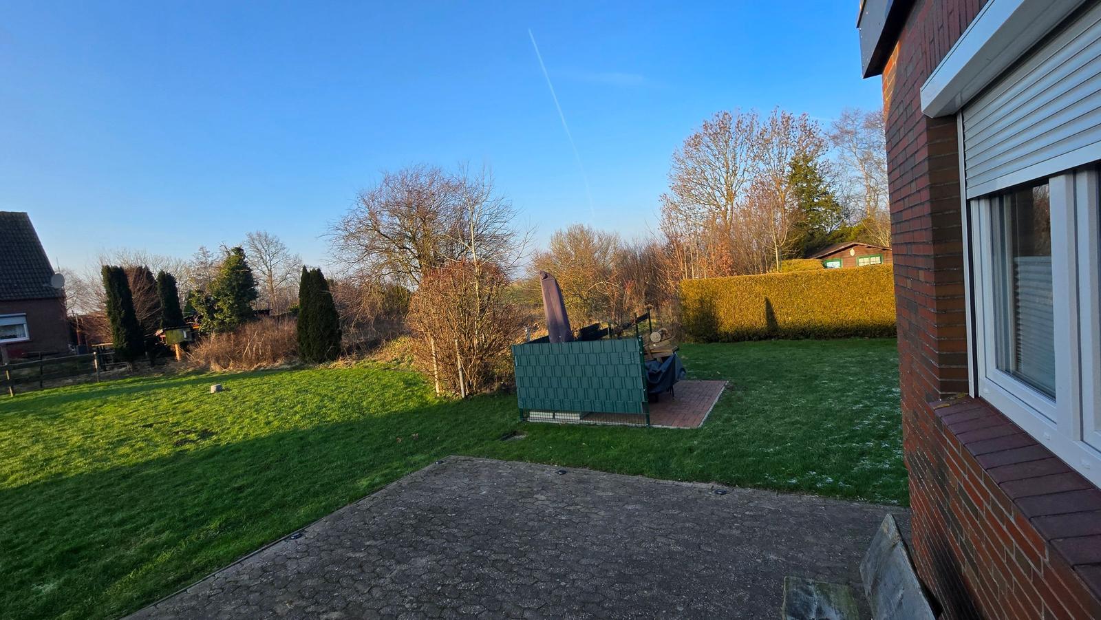 Hinterhof mit Rasen, Steinplatten und Gartenmöbeln. Blick auf Bäume und Nachbarhaus.