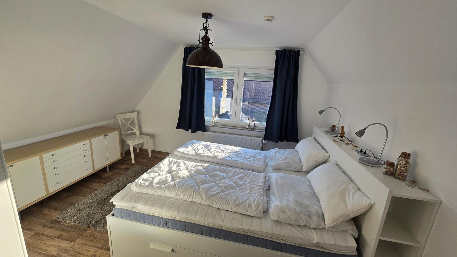 Schlafzimmer mit Doppelbett, Schrank und Fenster mit Vorhängen.
