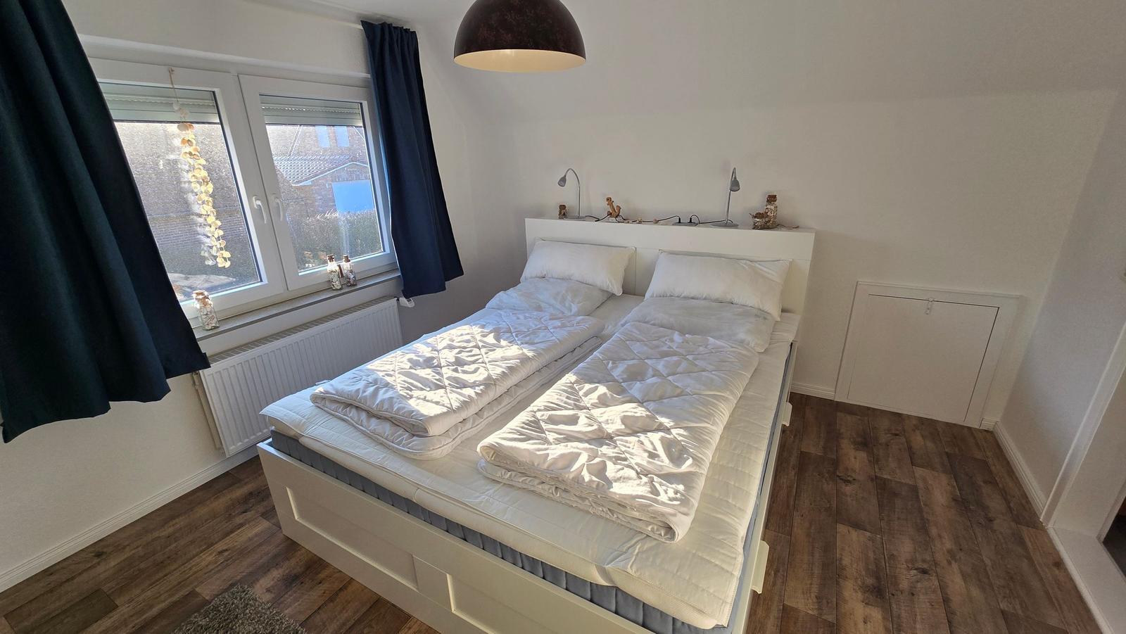 Schlafzimmer mit Doppelbett, Fenster und Holzboden.