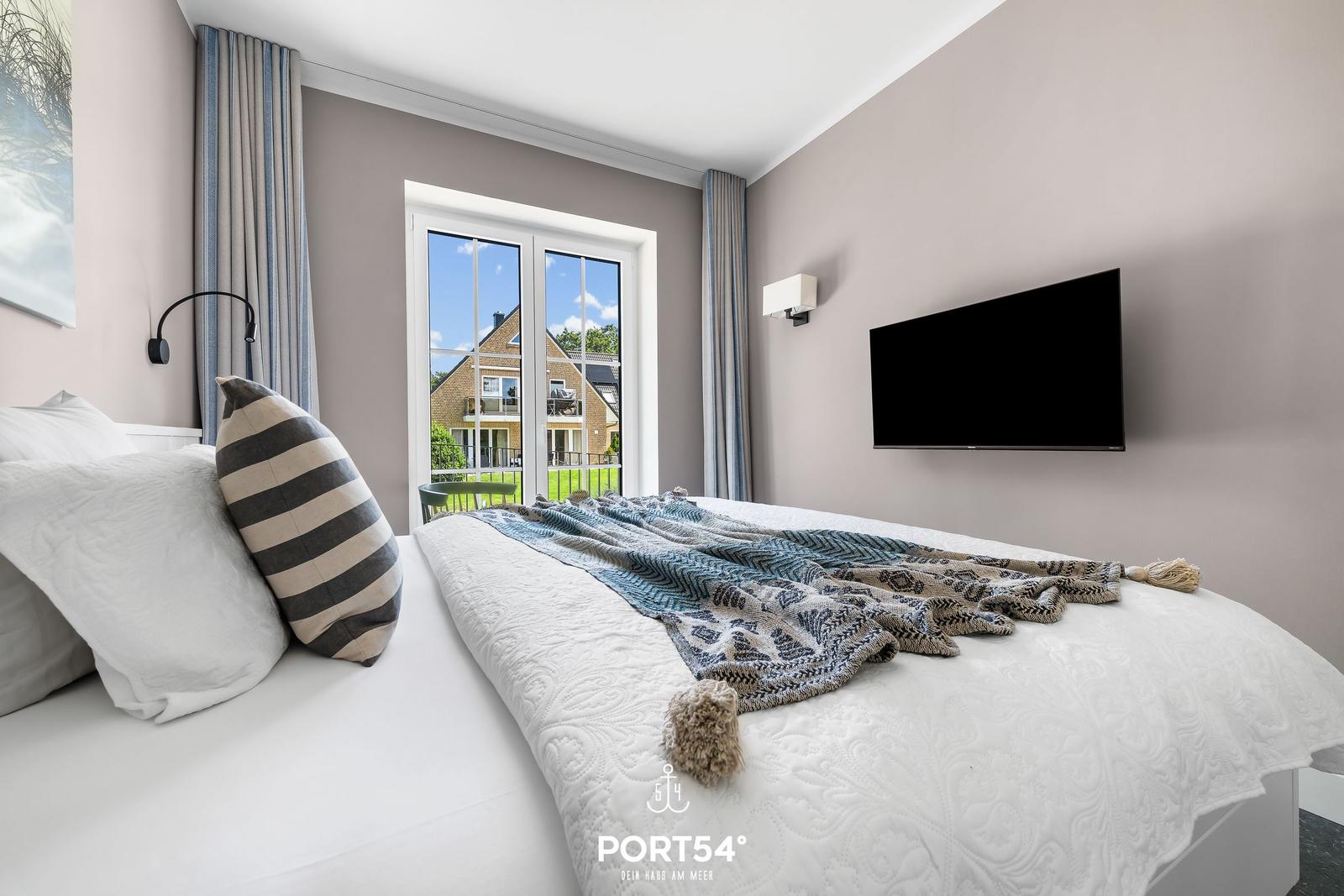 Schlafzimmer mit Bett, TV und Fenster zum Balkon.