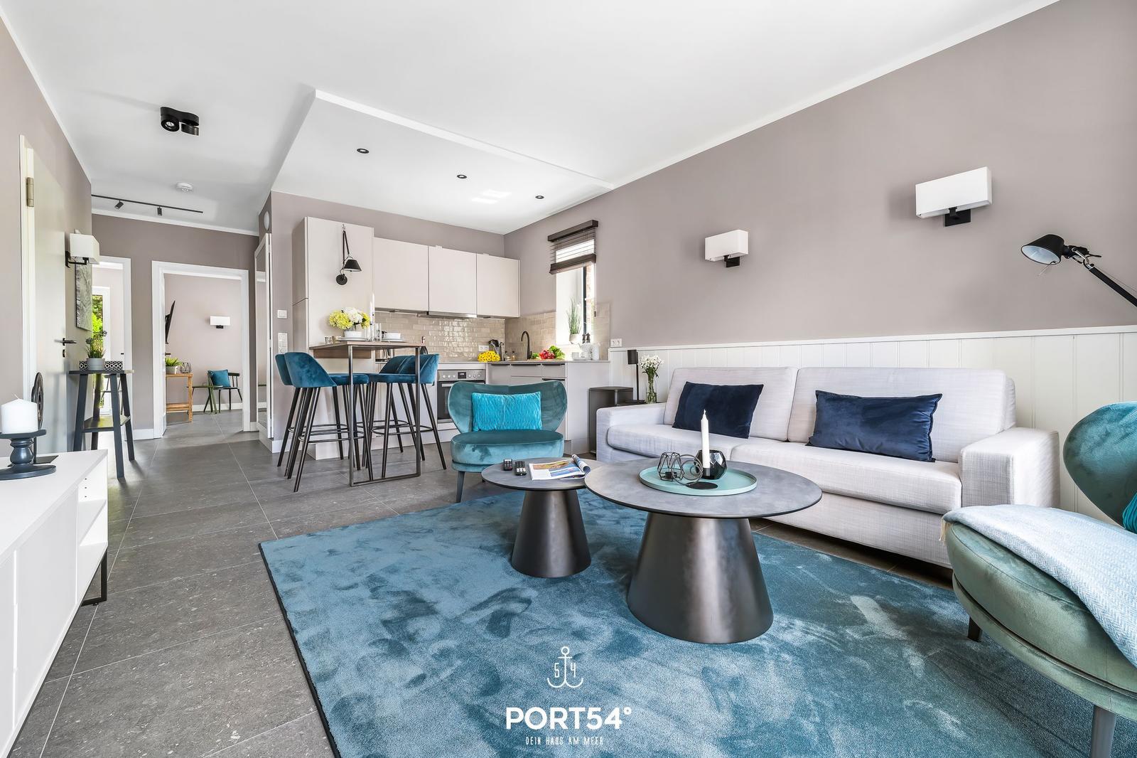 Wohnbereich mit Sofa, Sitzgelegenheiten und Küchenbereich im Hintergrund.