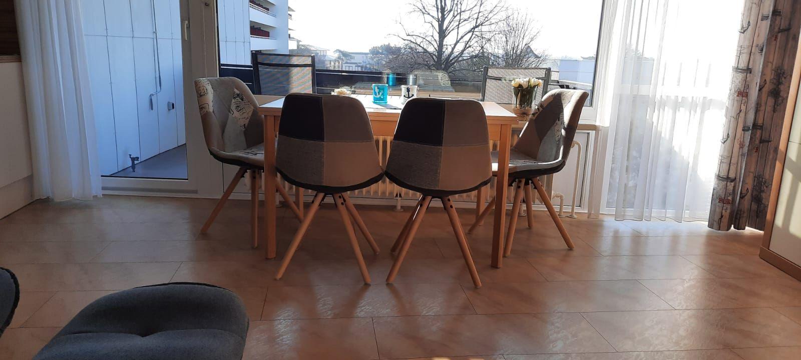 Esstisch mit vier Stühlen vor großem Fenster mit Blick auf Balkon.