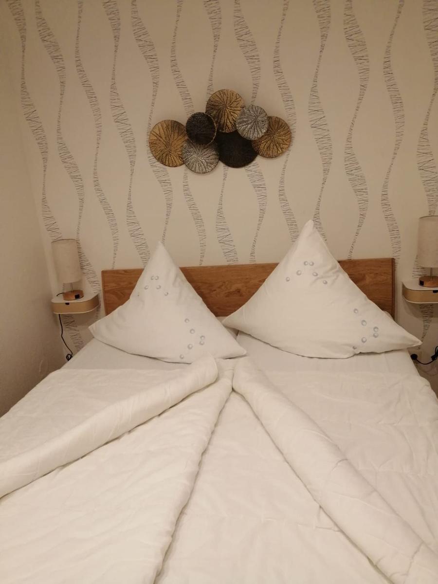 Doppelbett mit weißen Kissen und Decke, Wand mit Muster und Dekoration.