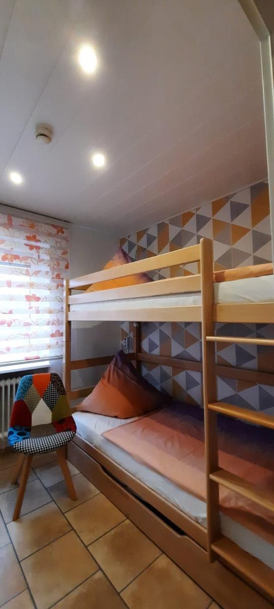 Zimmer mit Doppelstockbett, buntem Stuhl und gemusterter Wand.