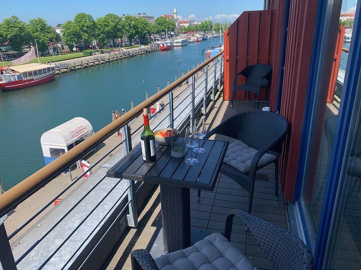 Terrasse mit Tisch, Stühlen und Blick auf Fluss und Boote.