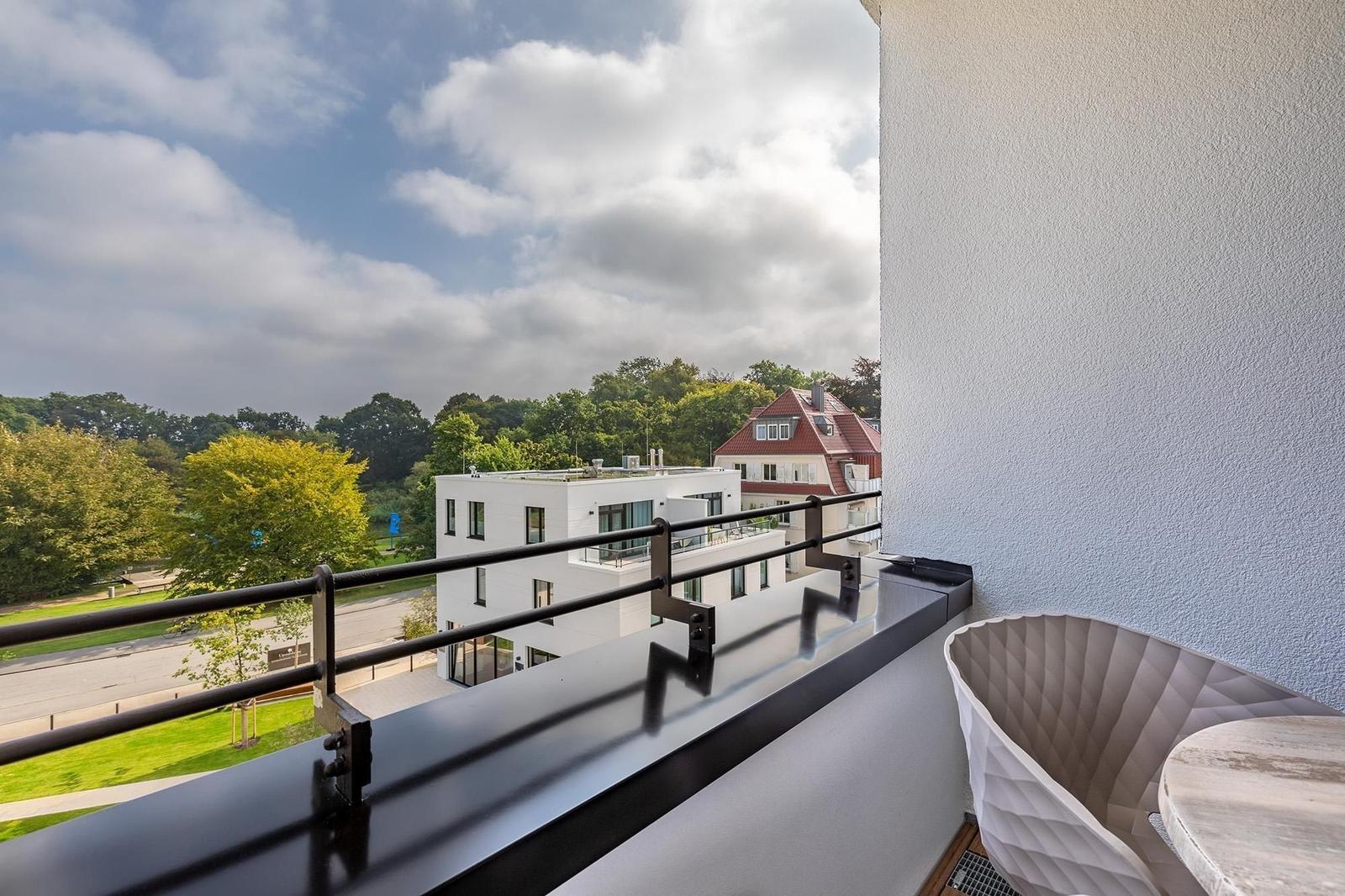 Balcony with modern chair overlooking green park and buildings.