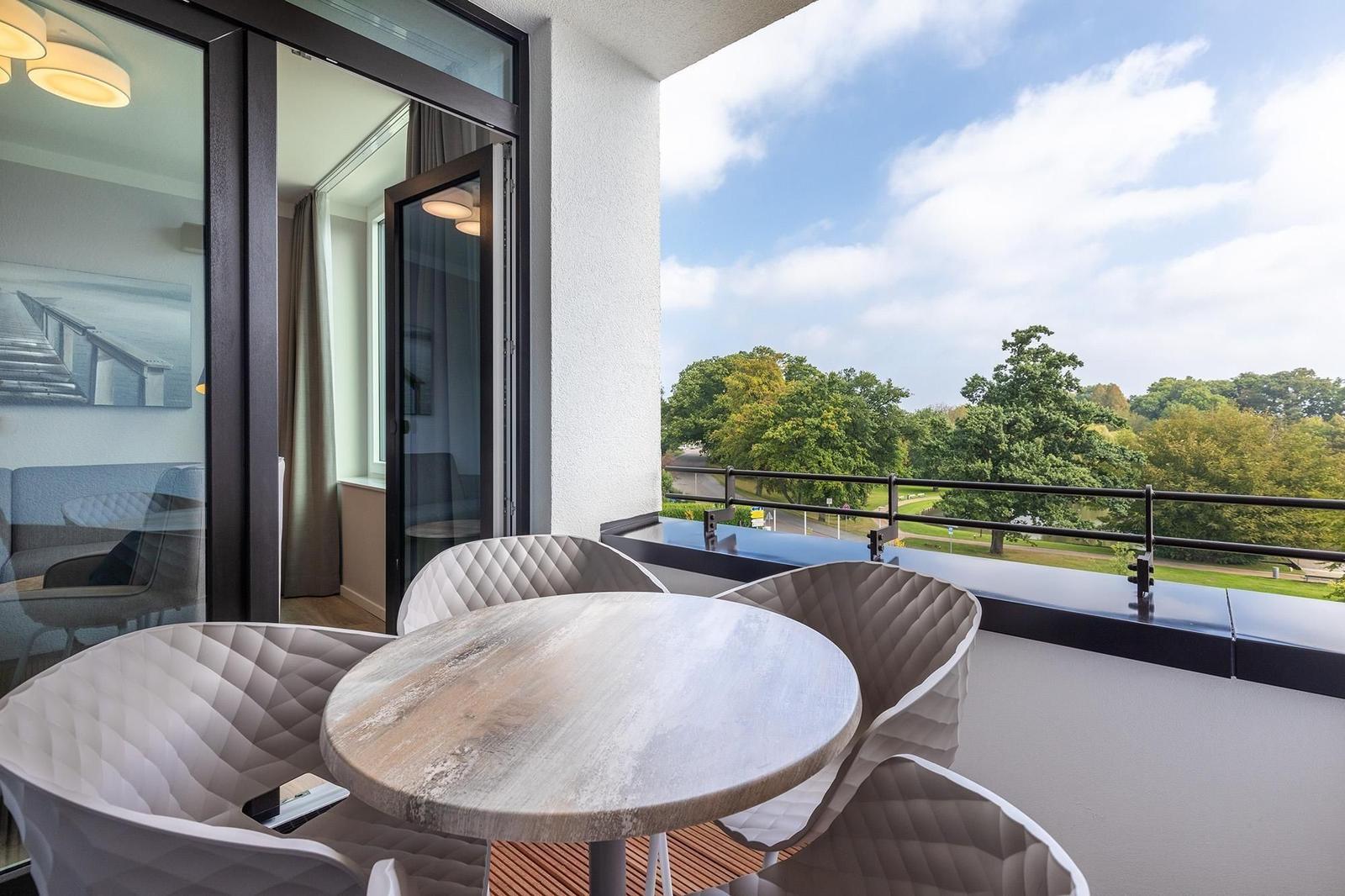 Balcony with table and chairs, view of green trees and sky.