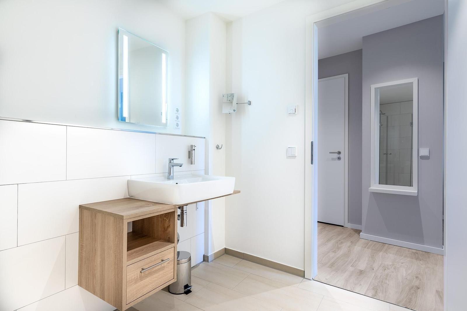 Badezimmer mit Waschtisch und Spiegel. Durchgang zur Dusche.
