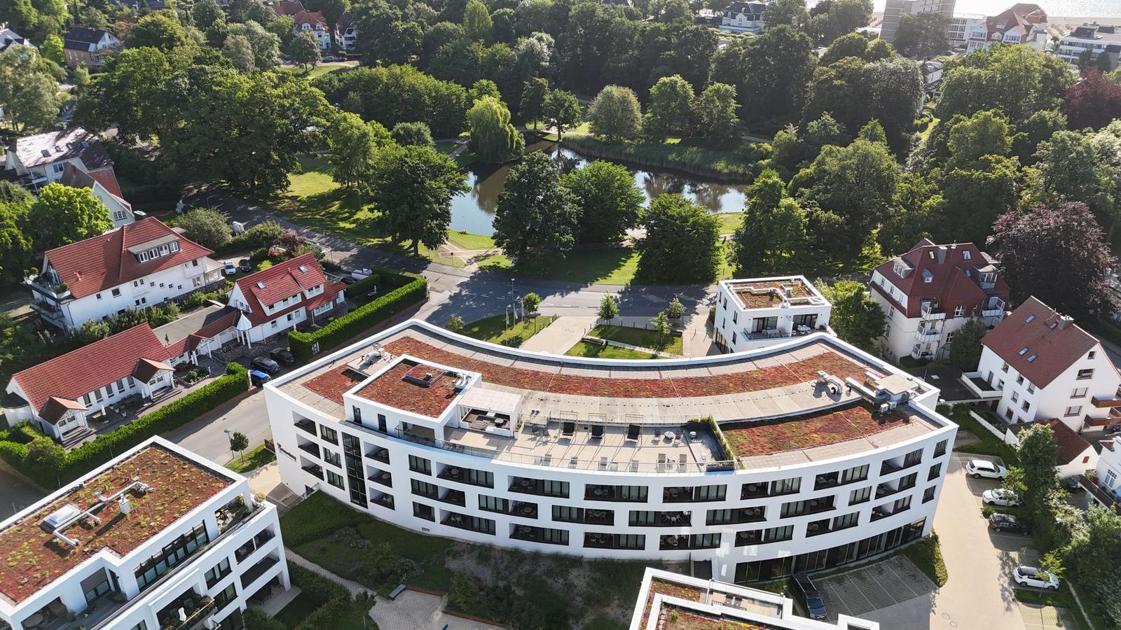 Moderne, weiße Wohnanlage mit begrüntem Dach und Blick auf einen Fluss und Bäume.